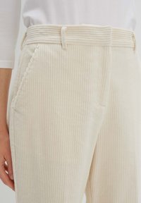 Hellbeige Cordhosen mit vertikalen Rippungen, ausgestattet mit einer taillierten Taille, Gürtelschlaufen und Seitentaschen. Weicher Stoff, lässiges Design.