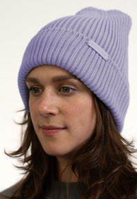 Gorro de punto lavanda con textura acanalada, que presenta una pequeña etiqueta con el nombre de la marca. El sombrero es suave y tiene un diseño holgado.