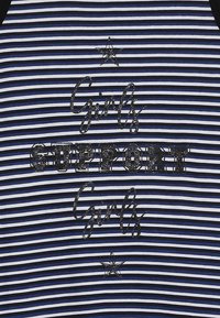 Paskowany materiał w kolorze granatowym i jasnoniebieskim z napisem "Dziewczyny WSPIERAJĄ Dziewczyny" w błyszczącym czarnym kolorze, z małymi gwiazdkami podkreślającymi wzór.