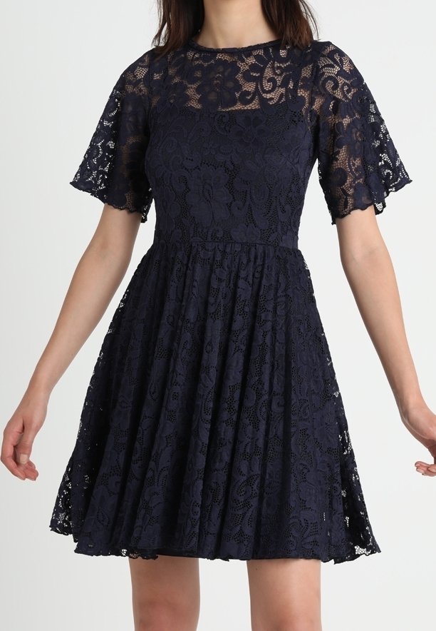 Marinblå spetsklänning med korta utsvängda ärmar, figurnära liv och utsvängd kjol. Har blommiga spetsmönster och fodrat liv för täckning.