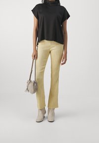 Top negro de manga corta, pantalones amarillos acampanados texturizados, bolso gris con lazos y botas beige hasta el tobillo. Elementos de diseño simples y modernos.