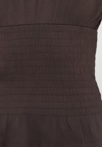 Καφέ ύφασμα με πτυχώσεις, διαθέτοντας οριζόντιες πιέτες στη μέση, που μετατρέπεται σε ομαλή κάτω περιοχή. Μαλακό και ελαφρύ υλικό.