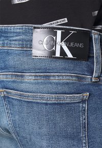 Jeans i denim med en ljusblå tvätt och mjuk textur. Har en svart läderpatch med "CALVIN KLEIN JEANS" och CK-logotyp på midjan.