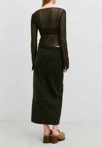 Schwarzes, durchsichtiges Langarmshirt, das über einem schlichten schwarzen Jeansrock mit luftiger Saumlinie und Gesäßtaschen getragen wird. Braune, hochhackige Clogs runden das Outfit ab.
