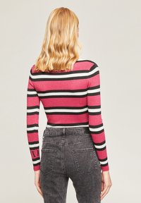 Haut ajusté à manches longues avec des rayures horizontales rouge, noir et blanc. Texture côtelée avec un col rond et un accent de logo sur la manche.