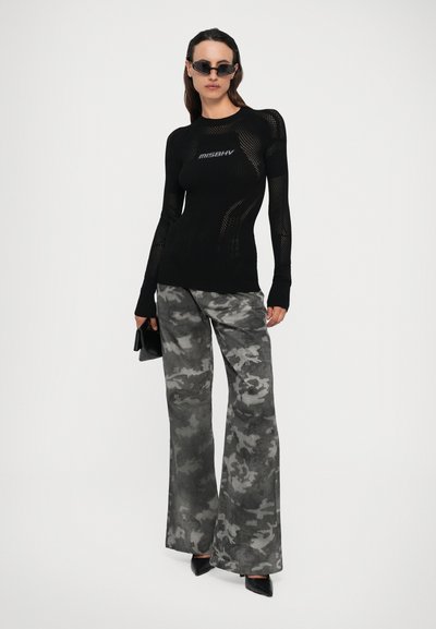 Haut noir en laine à manches longues avec des détails en maille et logo "MISBHV", associé à un pantalon large en camouflage gris et des escarpins noirs à bout pointu.