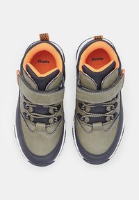 Sneaker per bambini verdi e neri con accenti arancioni, dotati di una fascia in velcro, lacci e materiali testurizzati per grip e comfort.