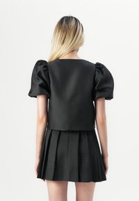 Svart cropped topp med pufferm og en glatt tekstur, kombinert med en plisserte svart miniskjørt, begge i en matt finish.