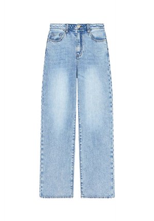 Mujer que lleva una camiseta blanca oversize, vaqueros anchos azul claro, sandalias negras de tacón alto, gafas de sol negras, sosteniendo un bolso negro.