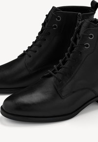 Bottines en cuir noir avec une finition lisse, devant à lacets et fermeture éclair sur le côté. Elles possèdent un bout rond et un design minimaliste.
