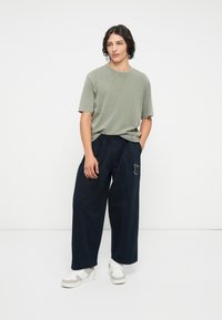 Gaiši zaļa īsām piedurknēm T-kreklā apvienots ar brīviem tumši ziliem biksēm, kurām ir dekoratīvs pielikums. Apģērbu noslēdz baltas kedas.