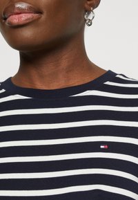 T-shirt rayé bleu marine et blanc avec un col rond et des manches courtes, arborant un petit logo de marque sur la partie gauche de la poitrine.
