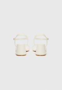White heeled sandals with wide, block heels and ankle straps. Smooth material with minimalistic design. Closed back and open toe.
