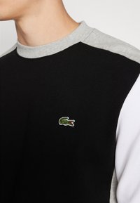 Felpa nera e grigia con girocollo e design a blocchi di colore. Presenta un logo di coccodrillo ricamato in verde sul petto. Tessuto in cotone.