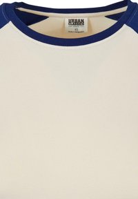 Biologisch katoenen T-shirt met een crèmekleurig lichaam en marineblauwe raglanmouwen. Zachte textuur, ronde halslijn en label zichtbaar aan de binnenkant van de kraag.