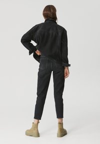 Black denim jacket with a relaxed fit, paired with black denim pants. Chunky olive green boots complete the outfit. Simple, minimal design.