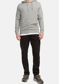 Hellgrauer Kapuzenpulli mit einer Fronttasche, verstellbarem Kapuzenzug und gerippten Bündchen, kombiniert mit schwarzen Hosen und grauen Sportschuhen.