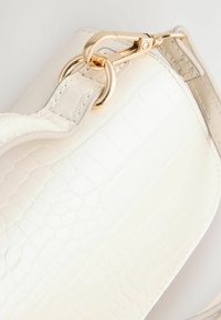 Borsa a tracolla in finta pelle bianca con motivo coccodrillo, dotata di hardware in tonalità oro, featuring un gancio a moschettone e anelli metallici per il fissaggio.