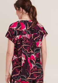 Maglietta a maniche corte, morbida e svasata, di colore nero, con vivaci motivi floreali rosa e arancio, caratterizzata da dettagli geometrici in contrasto e una consistenza morbida.