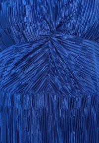 Mėlyna klostuota medžiaga su satino apdaila, su vertikaliomis ir įstrižomis klostėmis bei suktiniu dizainu juosmens srityje, lygi tekstūra.