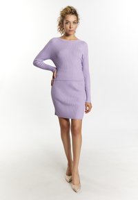 Lilafarbene gerippte Strickkleid mit langen Ärmeln und enganliegender Silhouette, mit einem Rundhalsausschnitt und nahtloser Taille, kombiniert mit beigen High Heels.