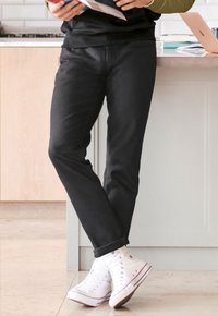Chino negre cu un croi drept și manșete răsucite, asortate cu adidași albi cu glezna înaltă; finisaj din material neted, detalii minime.