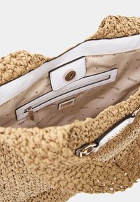 Sac à main en paille tissée beige avec une doublure blanche, comprenant une poche zippée et un fermoir en métal. L'intérieur présente un motif de marque "GUESS" répété.