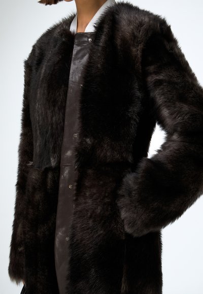 Manteau en fourrure brune foncée chaleureuse avec un devant en cuir lisse, doté d'un col montant et de boutons-pression, présentant une surface douce et texturée.