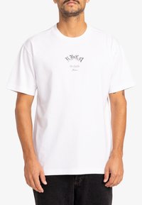 White cotton t-shirt with a round neckline and short sleeves. Features a black printed logo on the chest, simple and unembellished design.