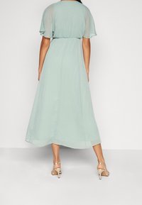 Une robe fluide de couleur menthe, fabriquée dans un tissu léger, avec de courtes manches volantées et une taille cintrée, dotée d'un ourlet à étages.