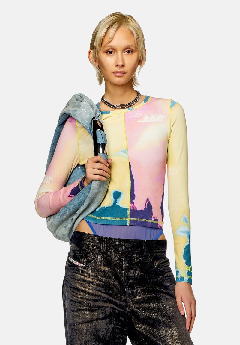 Kolorowy długi rękaw crop top z abstrakcyjnymi wzorami w kolorze różowym, żółtym i niebieskim. Połączony z ciemnymi, fakturowanymi spodniami high-waisted.