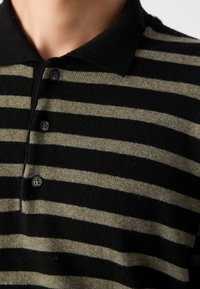 Gros plan d'un polo en maille rayé horizontal noir et gris avec un col et trois boutons noirs fermés à l'avant.