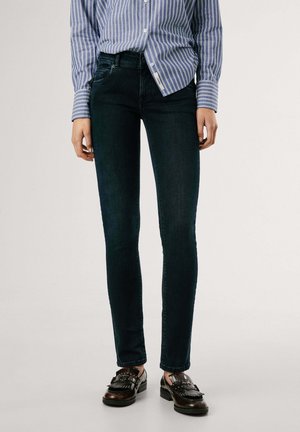 Jeans skinny de mezclilla oscura con un diseño de cinco bolsillos, que presentan una textura suave y un ligero estiramiento. Combinados con una camisa de botones a rayas azules.