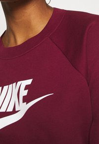 Marinröd sweatshirt med raglanärmar; har en iögonfallande vit Nike-logotyp över bröstet; mjuk tygtextur och klassisk rund halsringning.