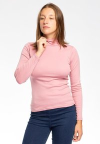 Maglietta rosa a maniche lunghe con colletto alto, realizzata in tessuto morbido e liscio, con un design aderente, abbinata a jeans di denim blu scuro.