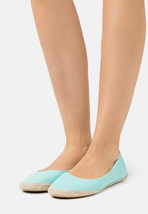 Sapatilhas de tela azul claro com bico redondo, apresentando uma sola de juta trançada. O design é minimalista, sem fechos ou adornos visíveis.