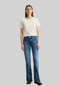 Roomkleurige t-shirt met korte mouwen gecombineerd met blauwe uitlopende denim jeans. De jeans hebben een aansluitende taille en een lichte vervaging voor detail. Zwarte schoenen maken de outfit compleet.