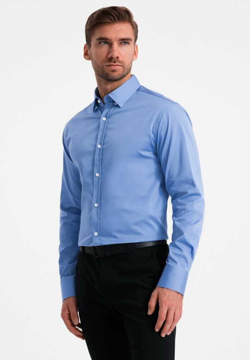 Lichtblauw overhemdd met een puntige kraag en lange mouwen, gecombineerd met zwarte broek. Heeft een gladde textuur en een getailleerd ontwerp.