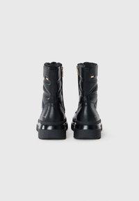 Juodi odiniai auliniai batai iki kulkšnies su tekstūruotu paviršiumi, šoninėmis užtrauktukais ir masyviu platformos padu. Sukurti su minkštu pamušalu ir minimaliais metaliniais elementais.