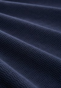 Donker marineblauw textiel met een textuur oppervlak, met subtiele golfpatronen en richels, gevouwen om diepte en dimensie te tonen.