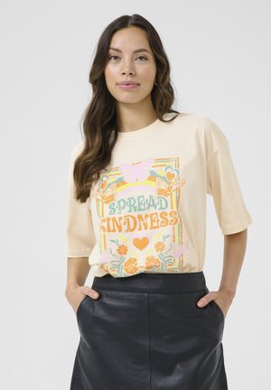 Camiseta beige de mangas cortas con un gráfico colorido que dice "Difunde Bondad", que incluye mariposas y flores. Combinada con una falda de cuero negra.