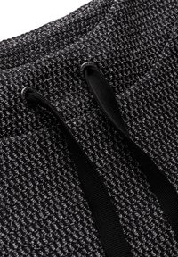 Texturiertes schwarzes Gewebe mit einem gewebten Muster, versehen mit einem Kordelzug und schwarzen Beschlägen. Nahaufnahme zeigt die Materialstruktur und Details.