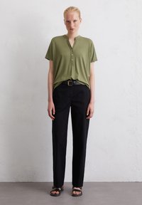 Olijfgroene henley shirt met korte mouwen en een knoopsluiting, gestopt in hoge zwarte broek; gecombineerd met zwarte sandalen.