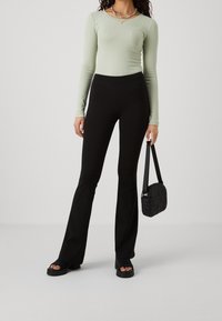 Ribbad långärmad topp i ljusgrön, i kombination med svarta utsvängda byxor. Accentuerad med ett färgglatt pärlhalsband och en texturerad svart handväska.