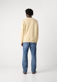 Lys gul sweatshirt med rund hals, kombinert med blå rette jeans. Stoffet ser glatt ut uten synlige mønstre.