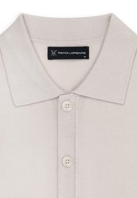 Jasno beżowa koszulka polo, mieszanka bawełny, z płaskim kołnierzykiem, zapinana na trzy guziki, z metką wszytą wewnątrz kołnierzyka.