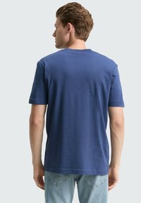 Granatowa, krótko rękawowa koszulka o prostym kroju, miękkiej fakturze i klasycznym okrągłym dekolcie, zestawiona z jasnymi dżinsami.