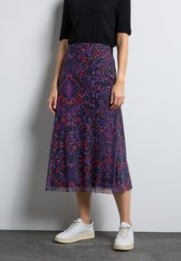 Uppflädd midikjol i mörk tyg med livliga lila och röda geometriska mönster. Kombinationen med vita sneakers ger en avslappnad stil.