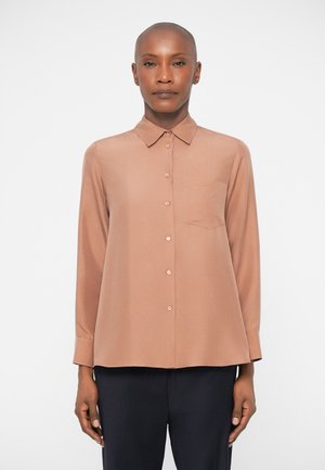 Blouse à manches longues, couleur brun clair, avec un col à boutons, une poche poitrine simple et une texture lisse. Les boutons discrets s'harmonisent avec la couleur du tissu.