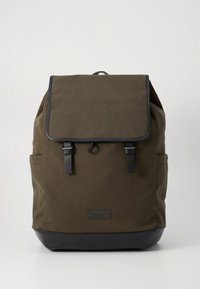 Πράσινο σακίδιο καμβά με μαύρο πάτο, με κλείσιμο με καπάκι, ρυθμιζόμενους ιμάντες και πλαϊνές τσέπες για αποθήκευση.